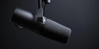 Un microfon de studio negru, suspendat, vazut de aproape, din lateral, pe fond cenusiu